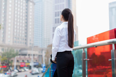 Thoughtful young businesswoman standing by railing in city