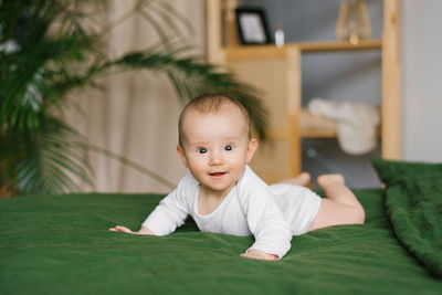 Cheerful smiling six-month-old baby in a bodysuit lies on his stomach on a cozy bed