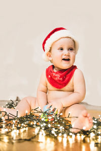 Cheerful baby boy sitting with illuminated christmas lights on floor