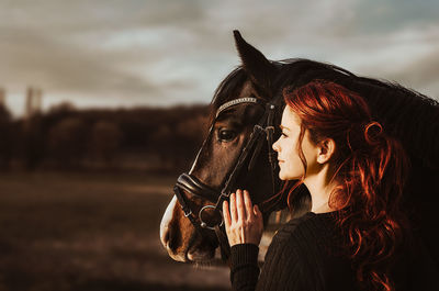 Two heads one love stallion with head collar and redhead woman are bonding