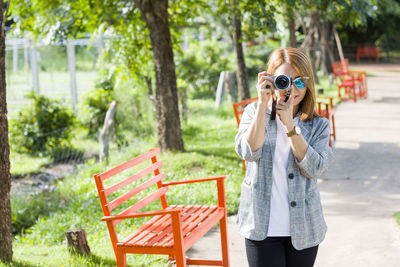 Young woman photographing while standing against trees