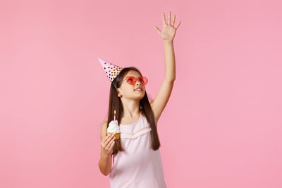 Young woman with arms raised standing against pink background