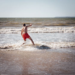 Rear view of shirtless man running at beach against sky