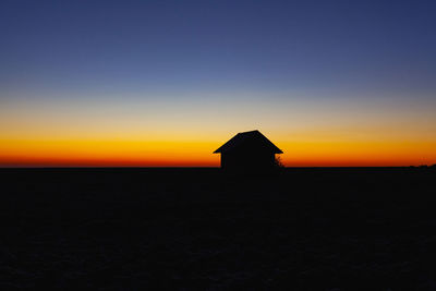 Silhouette house on land against sky during sunset