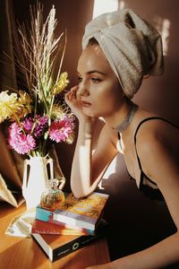 Portrait of young woman with red flowers in vase on table