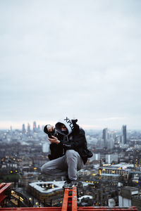 Woman photographing with cityscape in city against sky