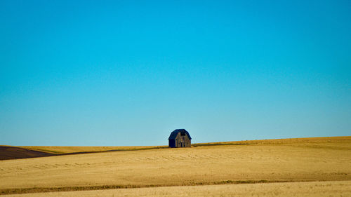 Scenic view of an abandoned barn on a field against clear blue sky