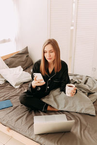 Young woman using mobile phone while sitting on bed