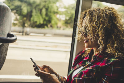 Woman using mobile phone by window in bus