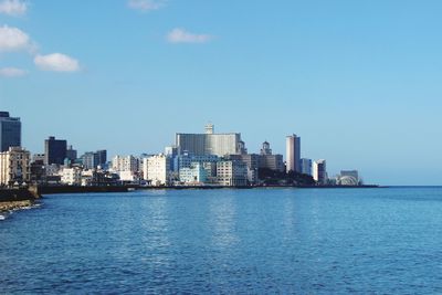Sea by buildings against blue sky