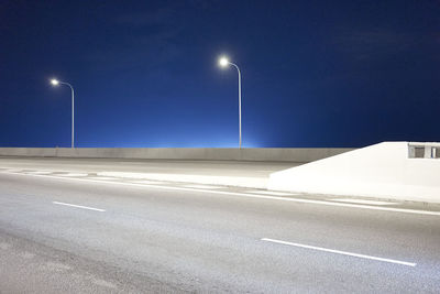 Empty road against clear blue sky at night