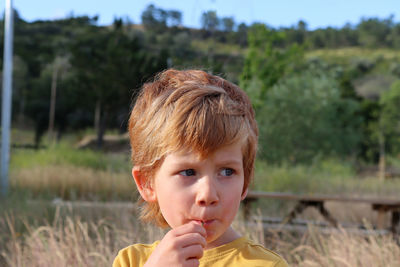 The blond boy holds a green branch in his mouth and draws in his cheeks.  