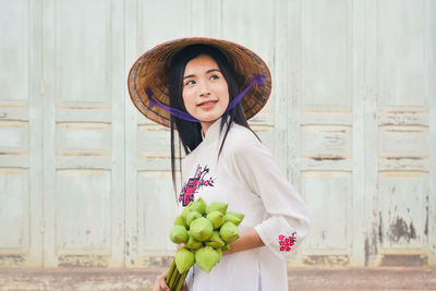 Beautiful woman wearing conical hat standing holding lotus buds