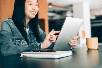 Young woman using mobile phone while sitting on table