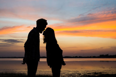 Silhouette man and woman standing against sky during sunset