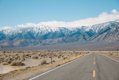 Road by mountains against sky during winter