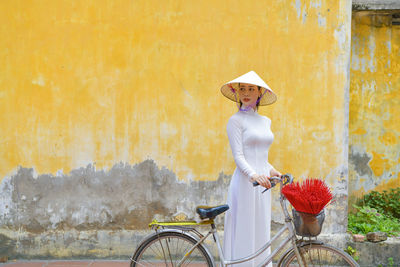 Side view of woman with bicycle against wall