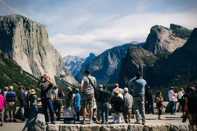 Tourists exploring amidst mountains against cloudy sky during sunny day