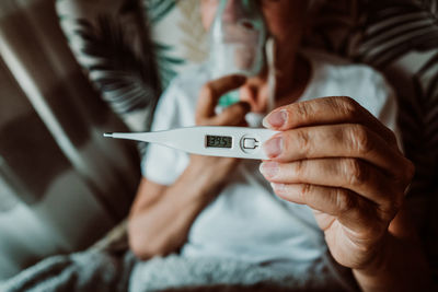 High angle view of senior woman holding thermometer while lying on bed at home