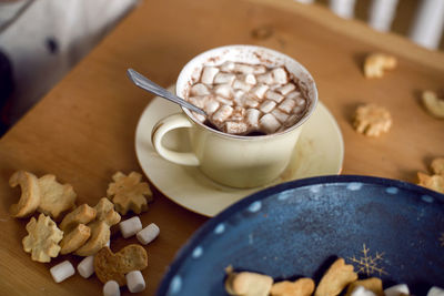 Ceramic mug with cocoa and marshmallow stands on a tray in the kitchen with cookies