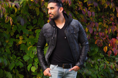 Young man standing with hands in pockets against plants at park