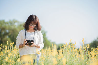 Woman photographing on field against clear sky