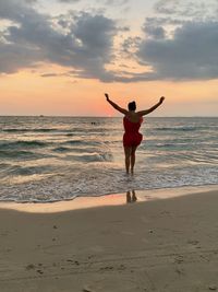 Rear view of boy on beach against sky during sunset