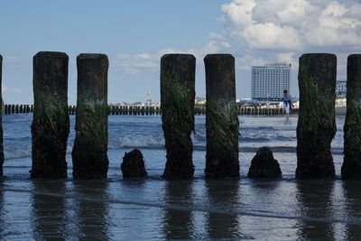 Wooden posts in sea against sky