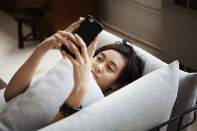 High angle view of young woman using smart phone while lying on sofa at home