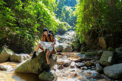 Woman holding map while sitting on rock in forest