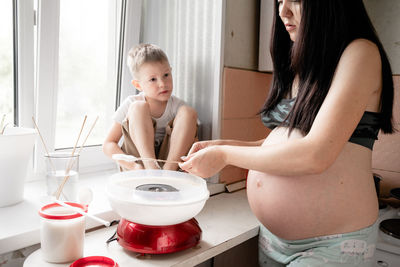 Pregnant mother with son making cotton candy at home