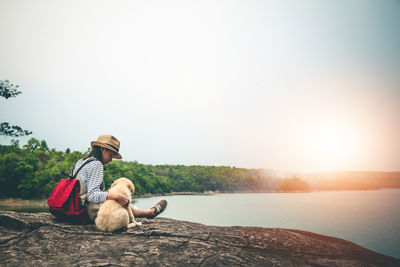 Woman sitting on rock looking at view against clear sky