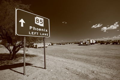 Road sign by street against sky in city