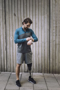 Young man with disability checking time while standing on footpath against wall