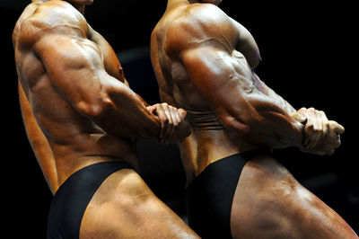 Midsection of shirtless men showing muscles while standing against black background