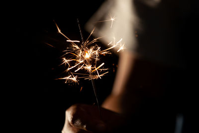 Cropped image of person holding sparklers against black background