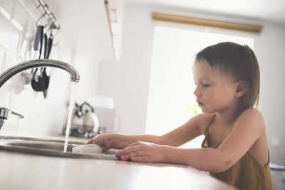 European child of 4 years old washes glass in sink on his own, bright kitchen in real interior, 