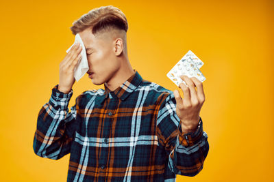 Young man looking away while standing against yellow background