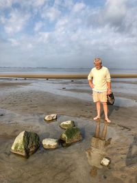 Full length of man standing on rock at beach against sky