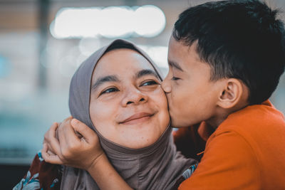 Cute boy kissing mother on cheek at home