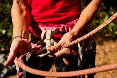 Cropped unrecognizable of active senior female tying rope on harness while preparing for climbing