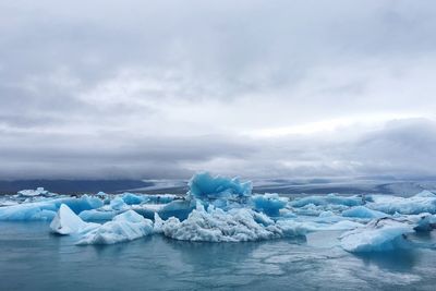 Scenic view of glacier in frozen lake against cloudy sky