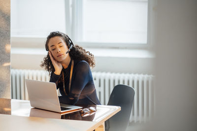 Young businesswoman wearing headset sitting with eyes closed at desk in office