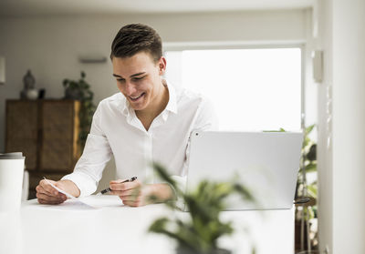 Happy young businessman reading document while sitting in home office