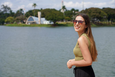 Portrait of young woman wearing sunglasses standing against lake