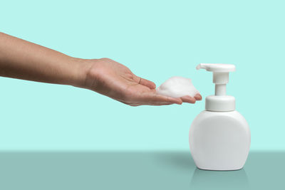 Close-up of hand holding bottle against white background