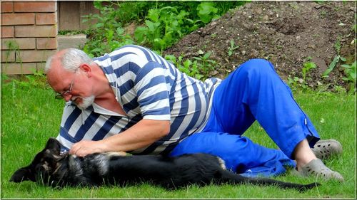 Full length of senior man playing with dog lying on grassy field