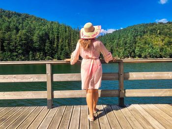 Back of woman wearing sun hat with the words wish you were here standing near a lake