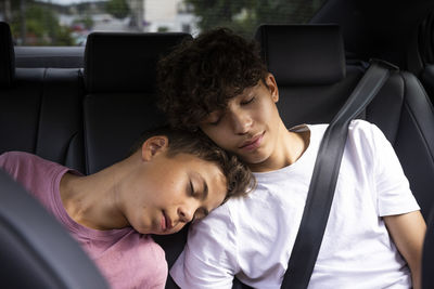 Tired brothers leaning on each other while resting in car