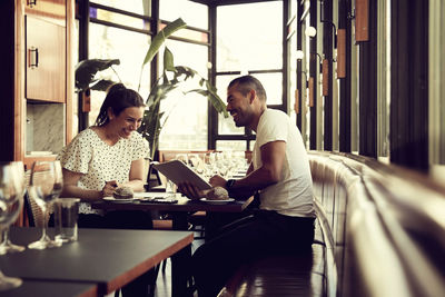 Smiling male and female with digital tablet sitting at table in cafe